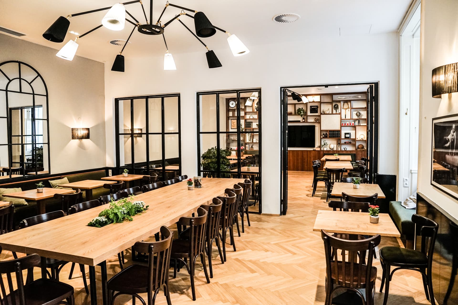 Heller Veranstaltungssalon mit langen Tischen und separatem Präsentationsbereich im Café Diglas